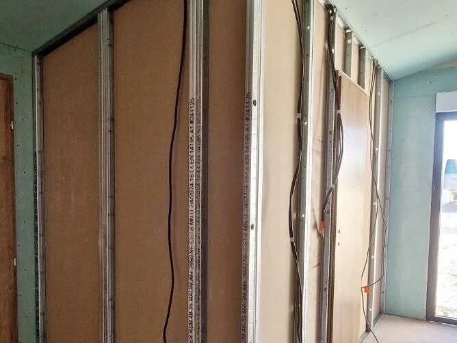 Cloison en cours de montage : ossature métallique, plaques de plâtre posées sur une face et câbles électriques en attente